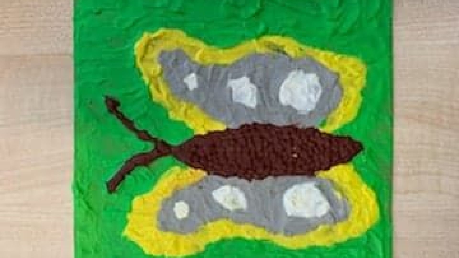 Praca wyklejona z plasteliny przedstawiająca brązowo-żółto-szaro-białym motylem na zielonym tle. Autor: Grzegorz S.