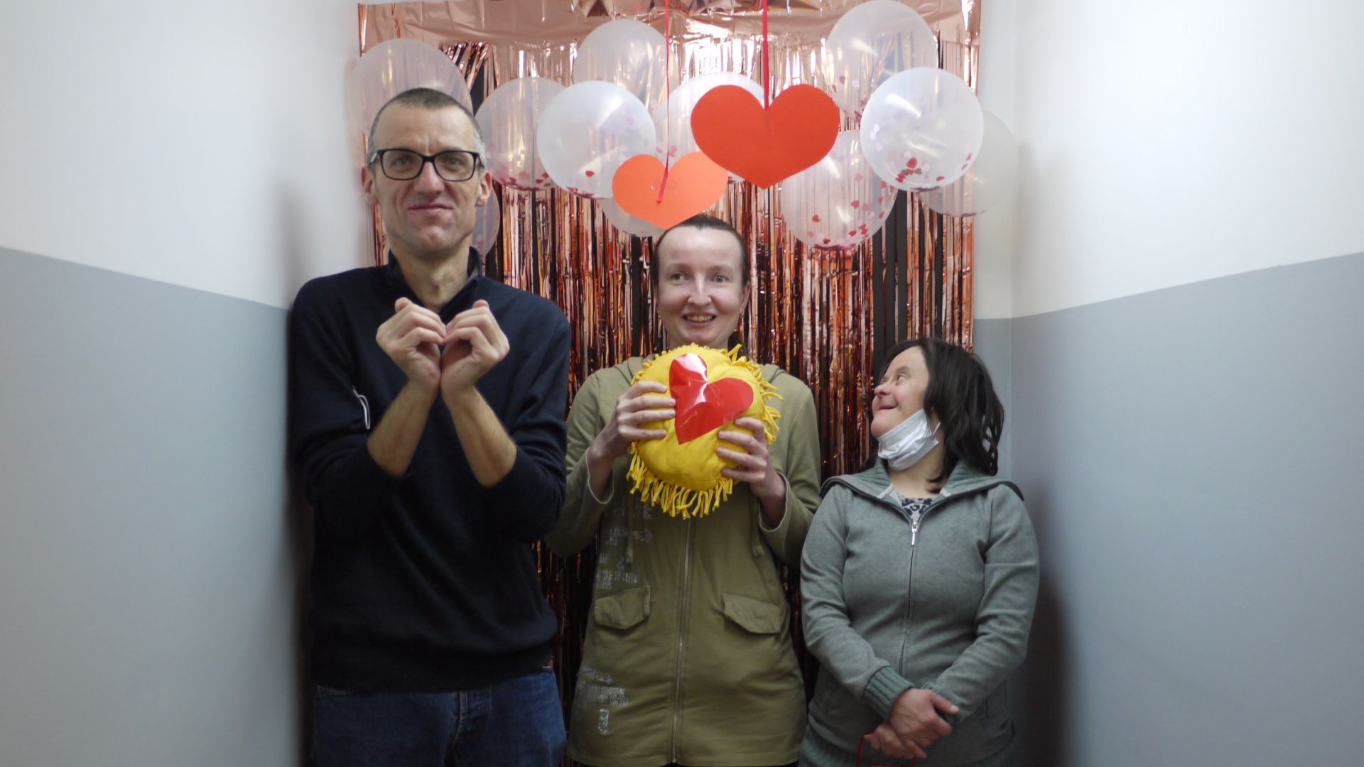 Grzegorz S., Anna Cz. i Agnieszka P. pozują na ściance udekorowanej balonami, serduszkami i serpentynami.