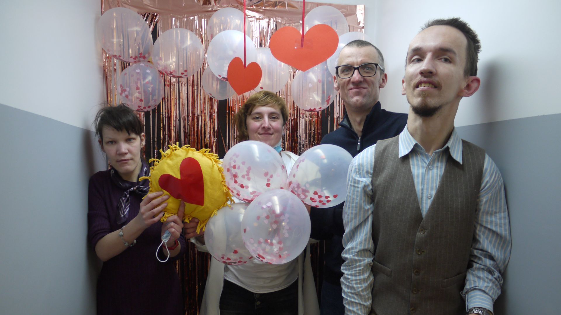 Uczestnicy pozujący na ściance udekorowanej balonami, serpentynami i serduszkami.
