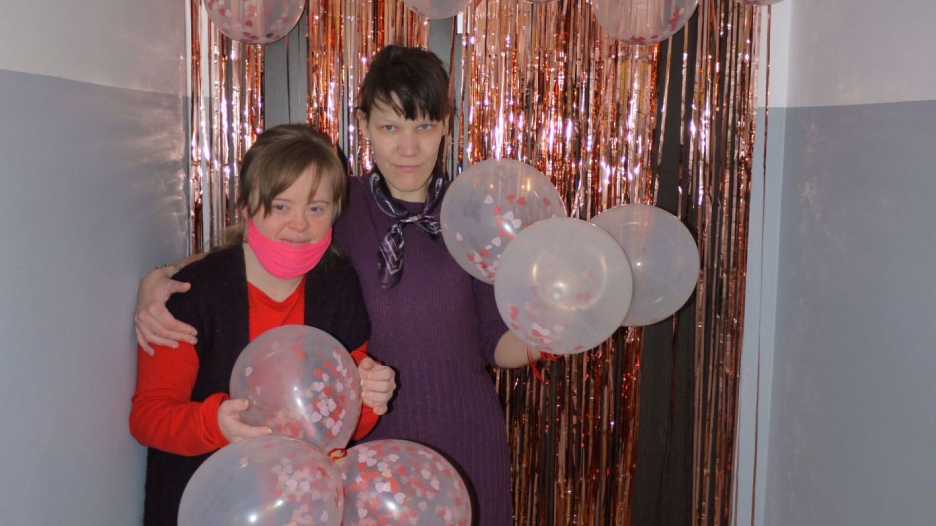 Martyna W. i Małgorzata W. pozujące na ściance udekorowanej serpentynami, balonami i serduszkami. W rękach trzymają balony.