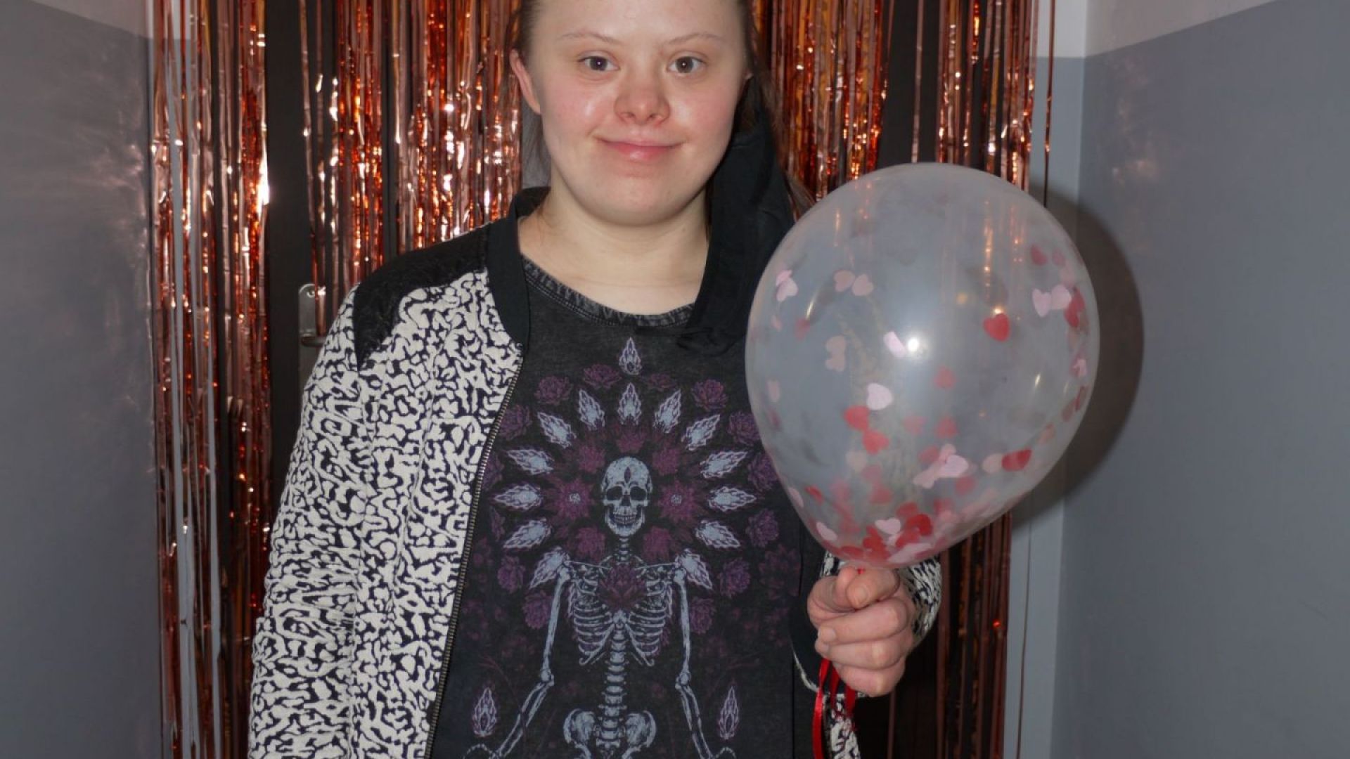 Marta Cz. pozująca z balonem w ręku na ściance udekorowanej balonami, serpentynami i serduszkami.