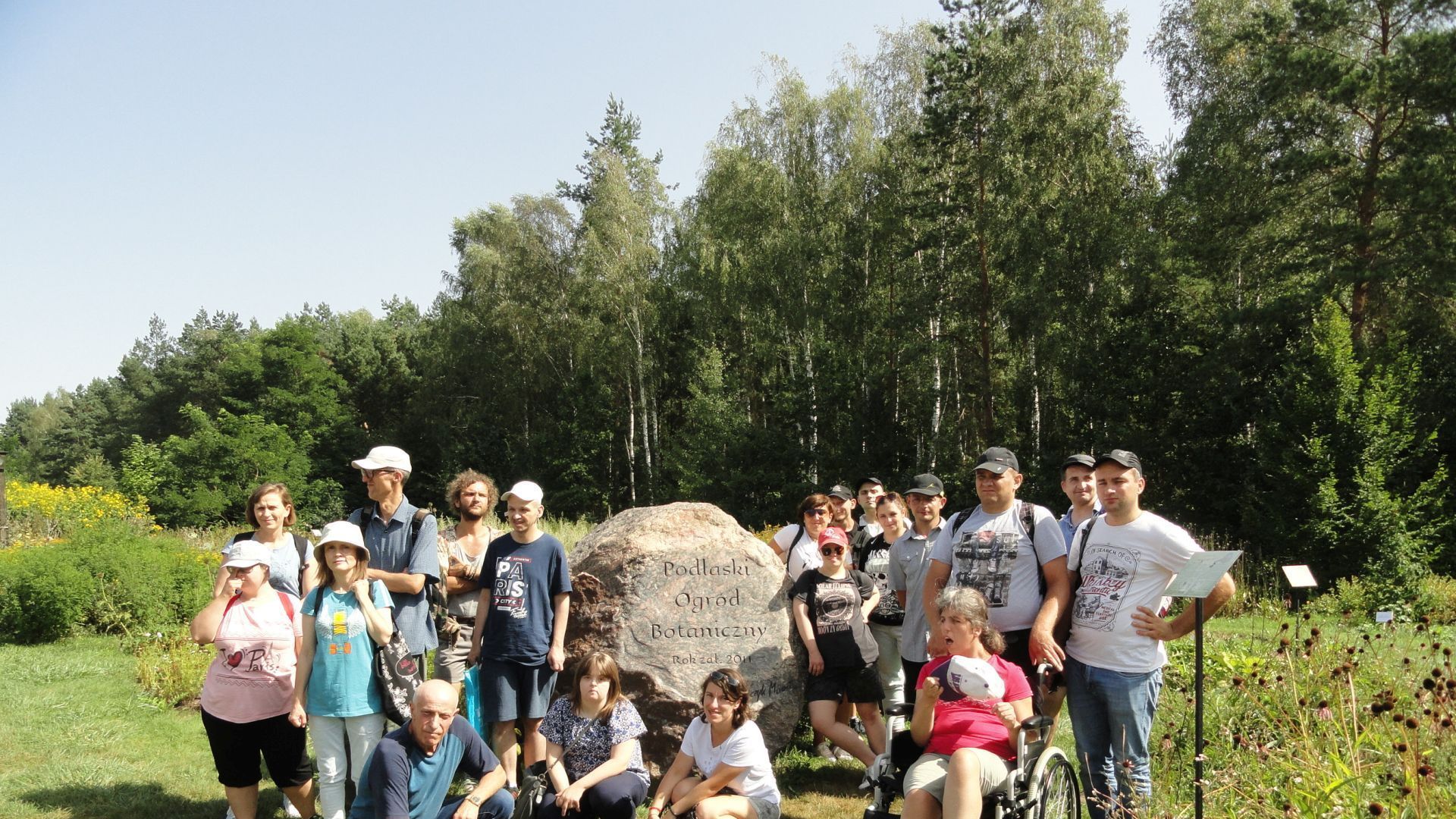 Uczestnicy wraz z opiekunami i przewodnikiem przy kamieniu z napisem Podlaski Ogród Botaniczny.