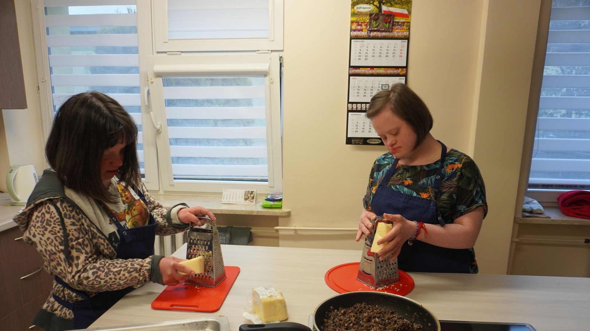 Uczestniczki Justyna i Marta ścierają ser podczas przygotowań do wspólnej kolacji.