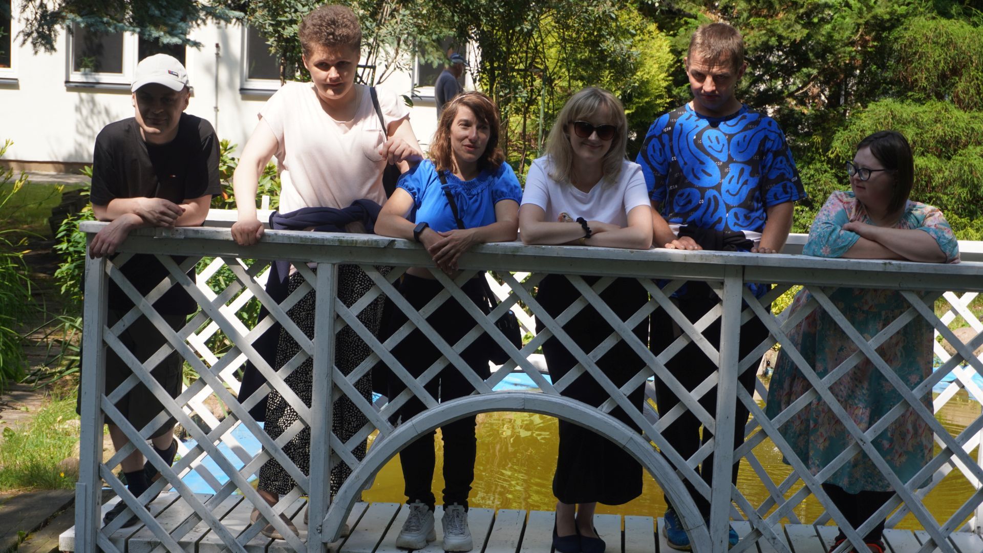 Uczestnicy wraz z terapeutą pozują do zdjęcia na drewnianym mostku podczas ''II Pikniku u Józefa''.