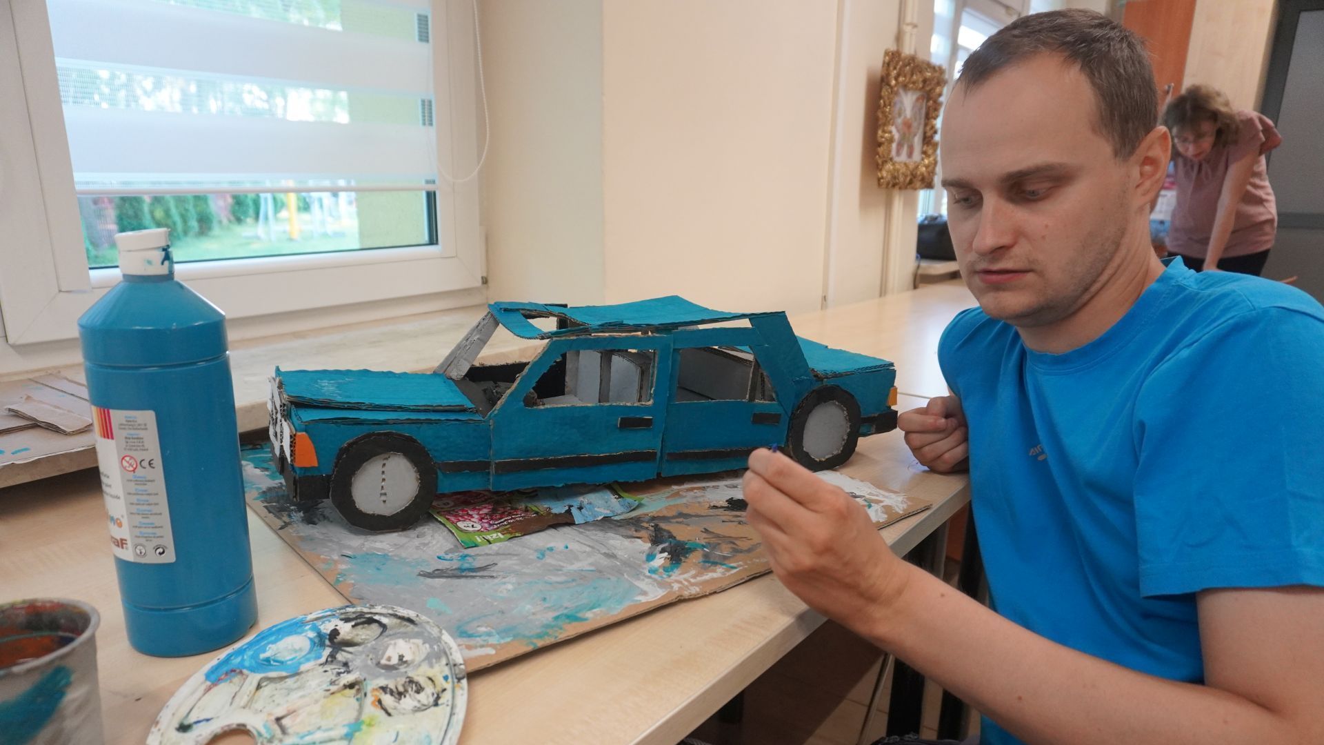 Galeria: Uczestnik Krzysztof pozuje do zdjęcia podczas wykonywania pracy z kartonu przedstawiającej samochód (model starego Mercedesa). 