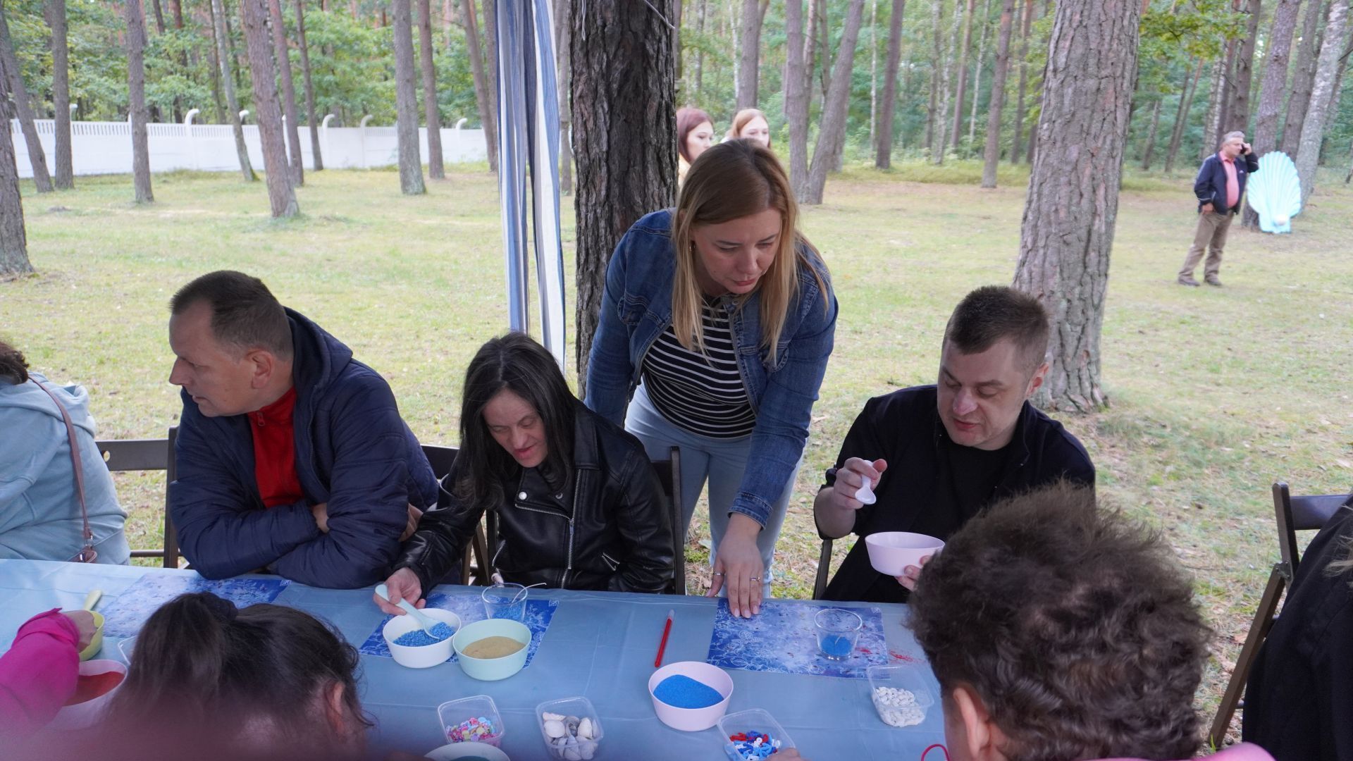 Uczestnicy z pomocą terapeuty robią świece żelowe podczas imprezy plenerowej ''Morskie Opowieści'' w DPS ''Jedlina w Mieni.