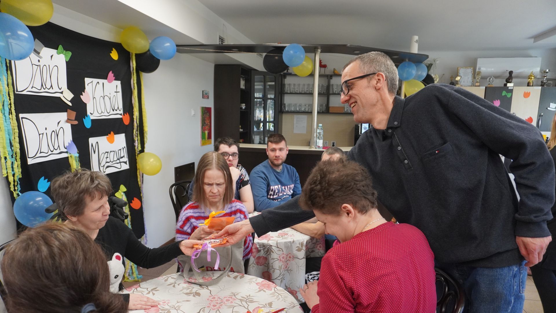 Uczestnik Grzegorz rozdaje upominki od Rady Domu z okazji Dnia Kobiet i Mężczyzn.