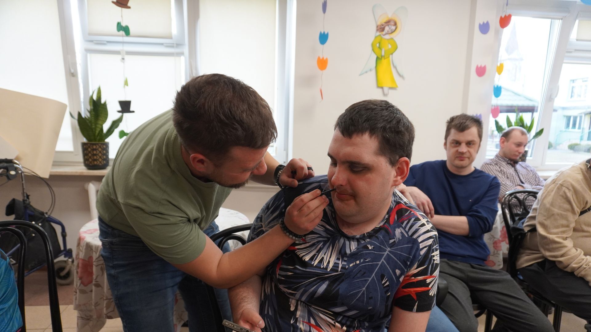 Uczestnik Bartłomiej wykonuje koledze Karolowi makijaż podczas zajęć integracyjnych z okazji Dnia Kobiet i Mężczyzn.