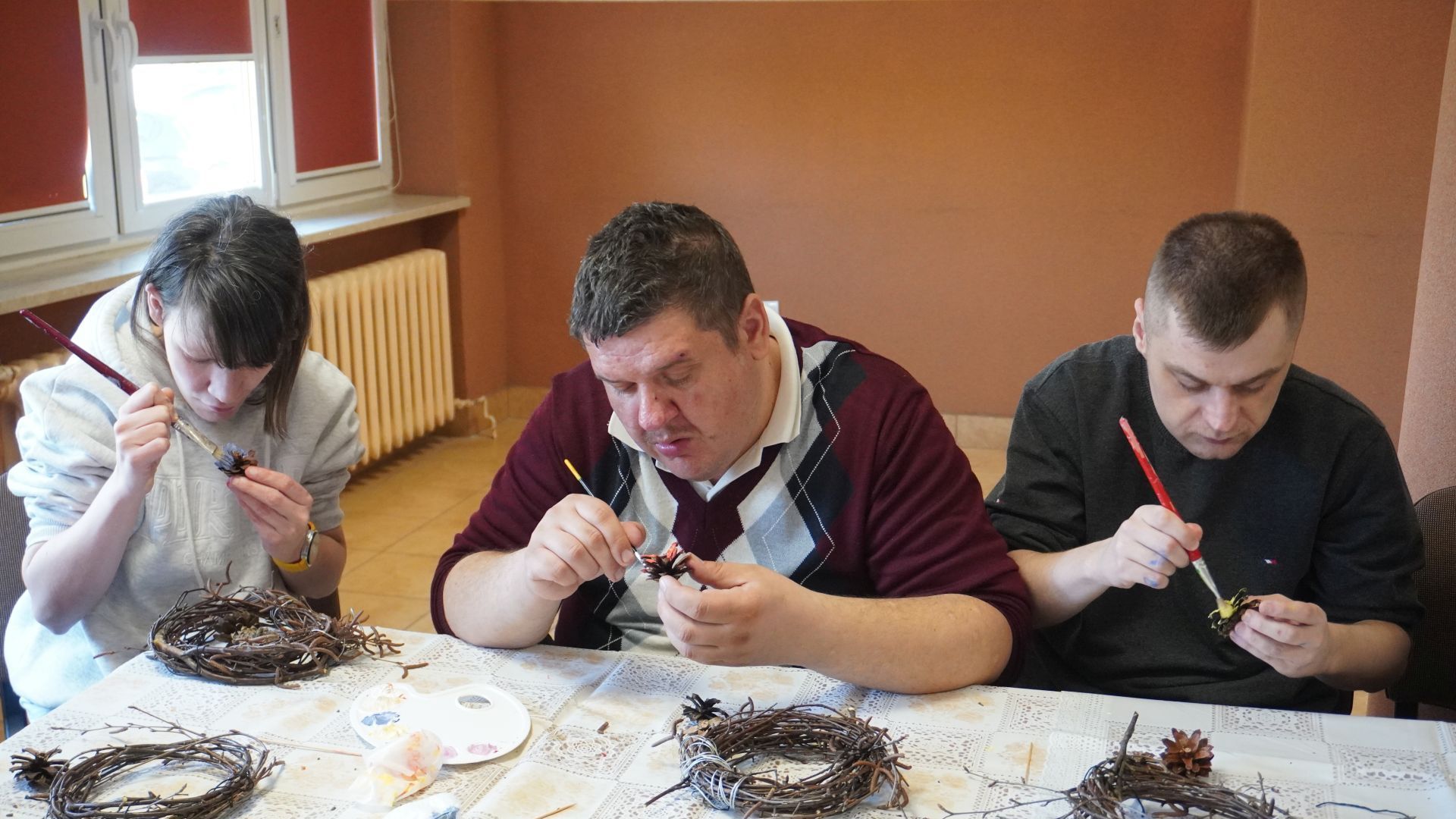 Uczestnicy malują szyszki podczas wielkanocnych warsztatów artystycznych.