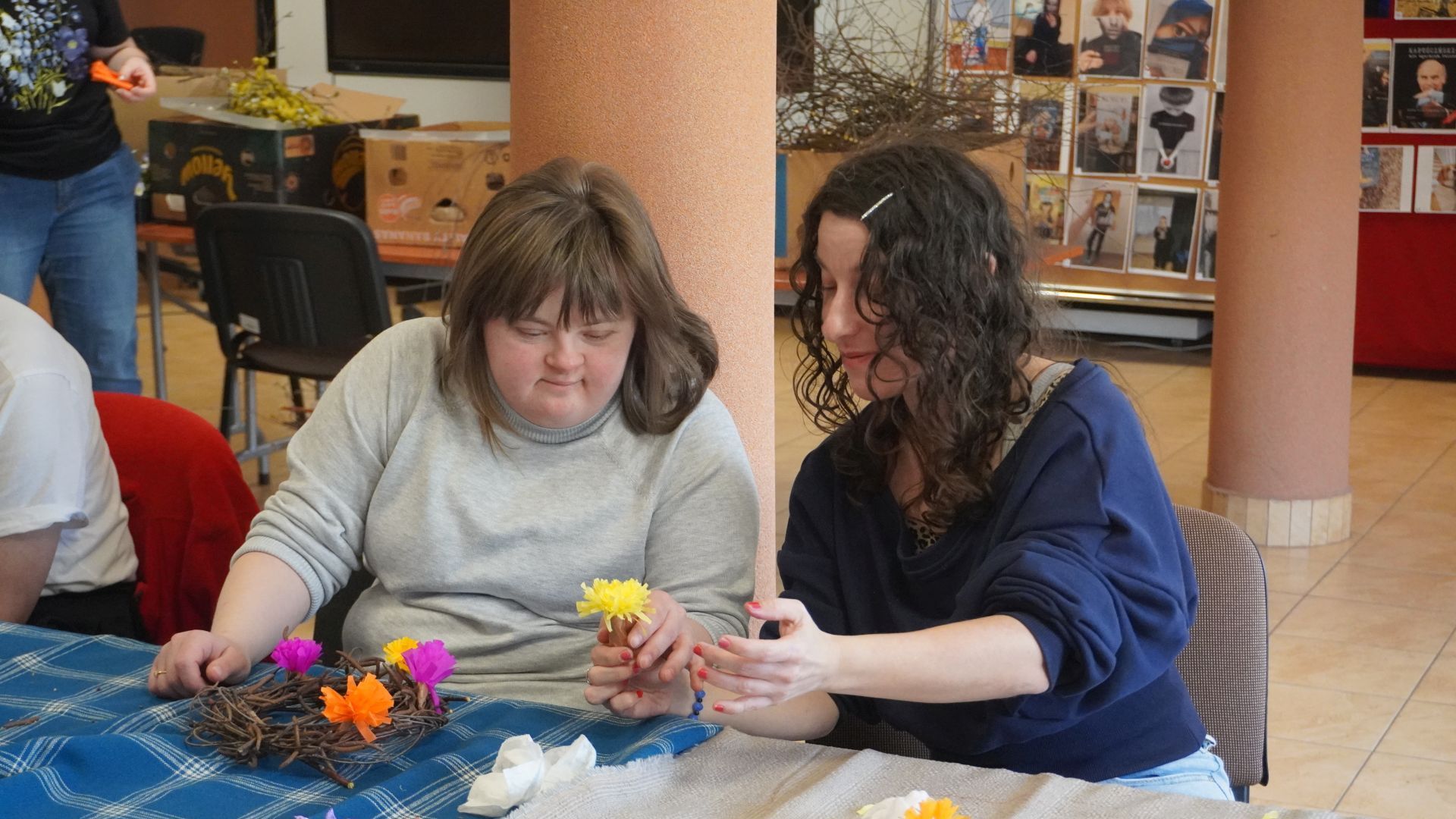 Uczestniczki Sylwia i Justyna K. robią kwiaty z bibuły podczas wielkanocnych warsztatów artystycznych.