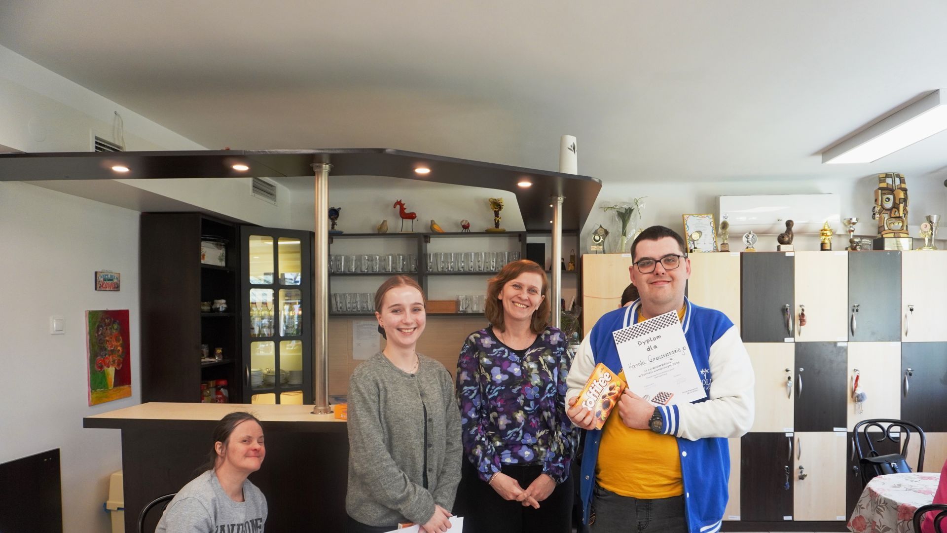 Uczestnik Karol odbiera dyplom i słodki upominek za zajęcie III miejsca w Turnieju Warcabowym 2026. 