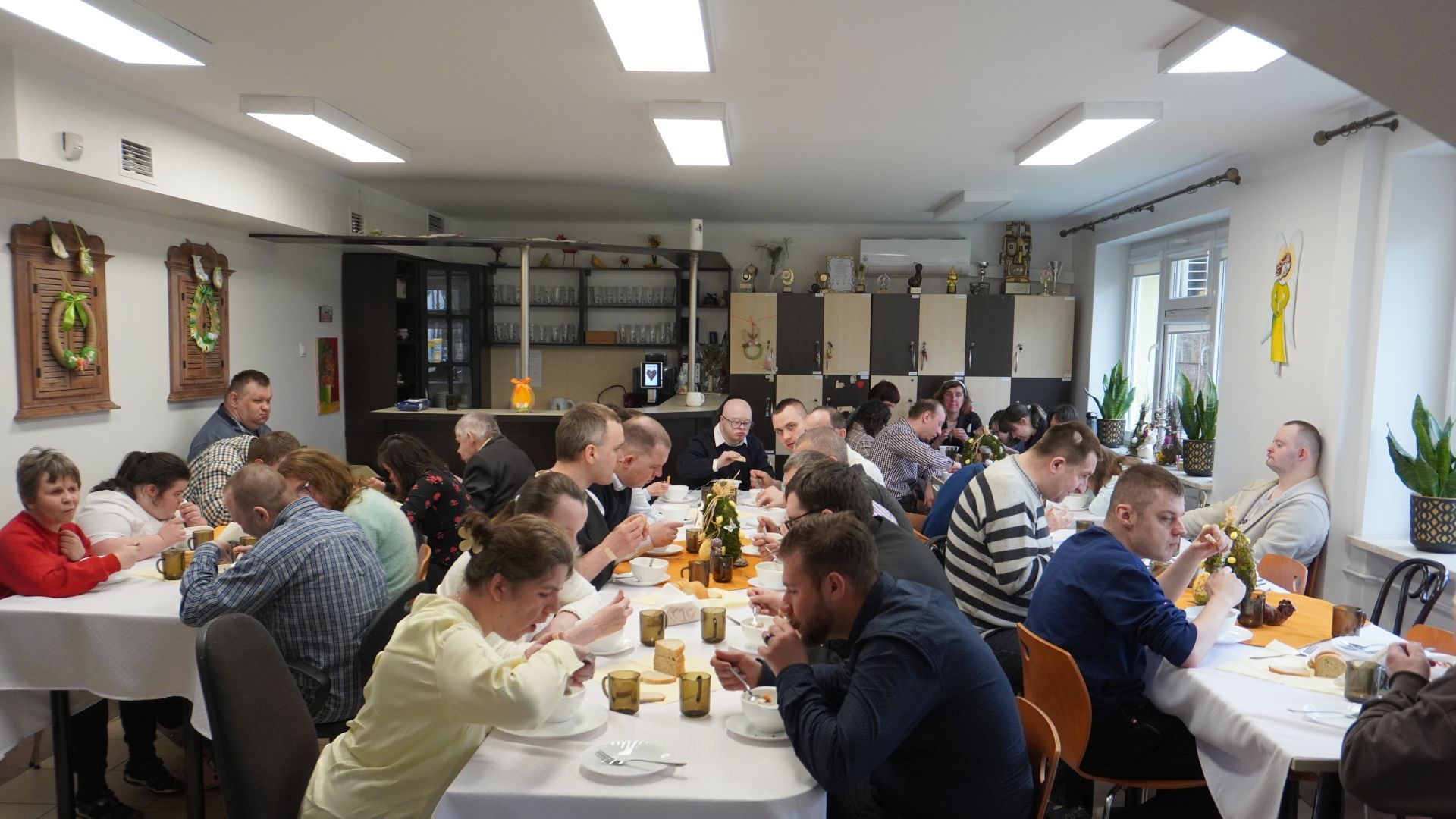 Uczestnicy siedzą przy stołach i jedzą żurek podczas spotkania wielkanocnego.