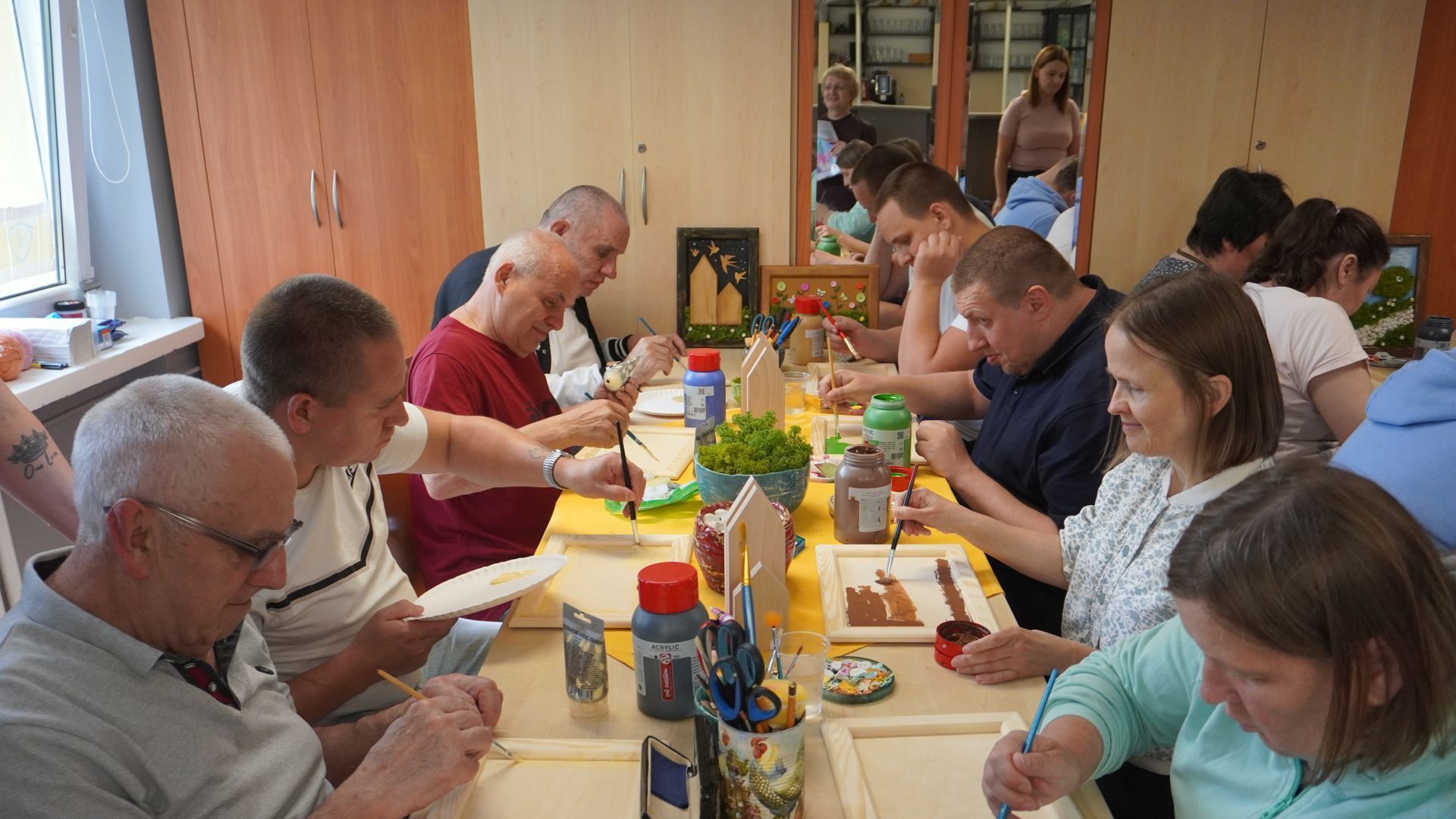 Uczestnicy malują drewniane ramki podczas warsztatów artystycznych Uczestnicy malują drewniane ramki podczas warsztatów artystycznych